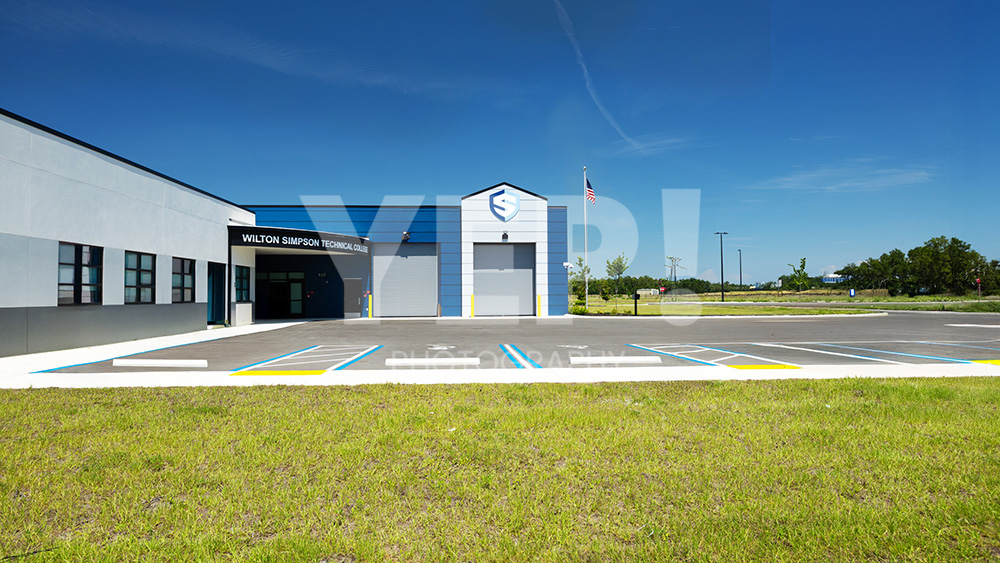 01-skanska-wilston-simpson-technical-college-yep-yepphotography-gabriel-gabrielaboujaoude-photography-realestate-interior-exterior Exterior view of the new Wilton Simpson Technical College building with parking lot under a clear blue sky