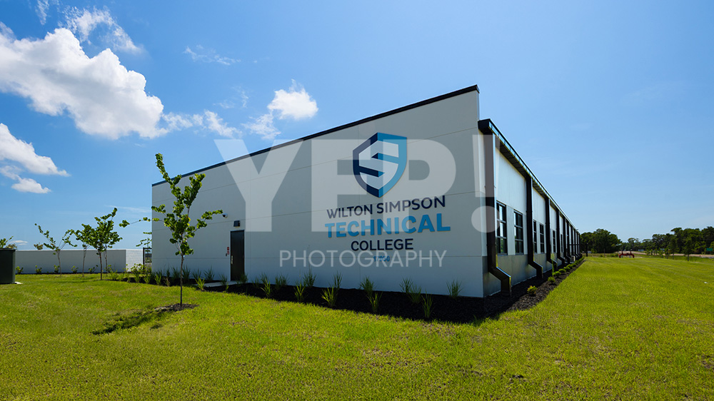 02-skanska-wilston-simpson-technical-college-yep-yepphotography-gabriel-gabrielaboujaoude-photography-realestate-interior-exterior Exterior view of the new Wilton Simpson Technical College building with parking lot under a clear blue sky