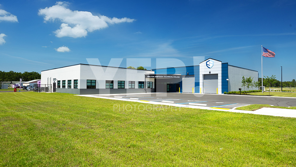 04-skanska-wilston-simpson-technical-college-yep-yepphotography-gabriel-gabrielaboujaoude-photography-realestate-interior-exterior Exterior view of the new Wilton Simpson Technical College building with parking lot under a clear blue sky